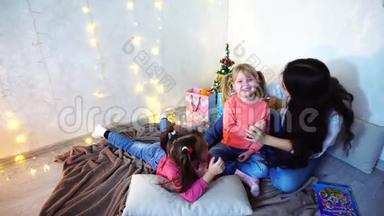 美丽的姐姐，在<strong>圣诞树和圣诞树</strong>的背景下，<strong>和</strong>坐在地毯上的小<strong>女孩</strong>玩耍